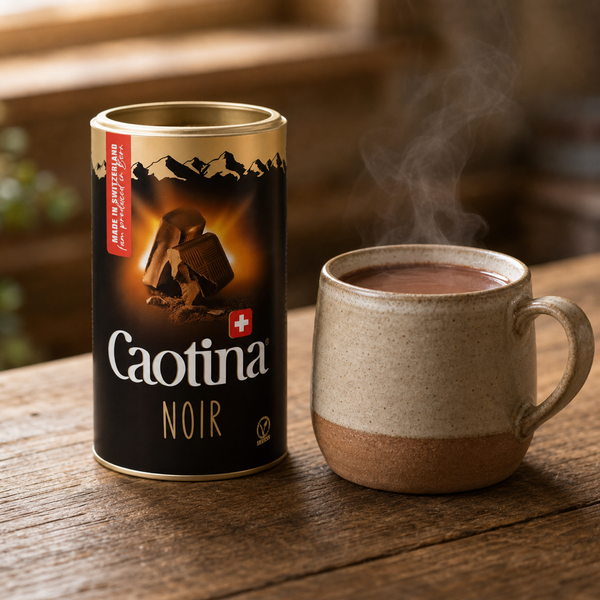 Caotina Noir Swiss dark drinking chocolate tin beside a steaming mug of hot chocolate